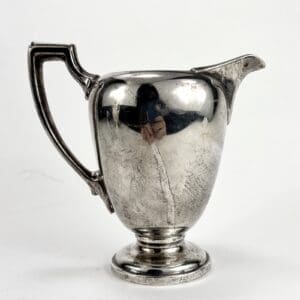 Silver pitcher with ornate handle and spout.