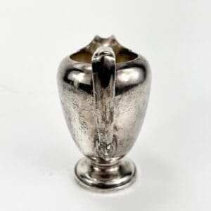 Silver creamer with ornate handle design.